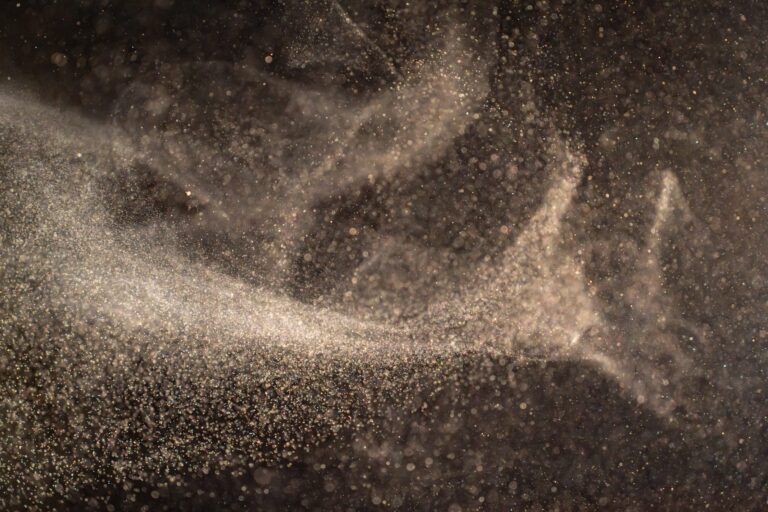 Organic dust particles floating on a light beam on black background.