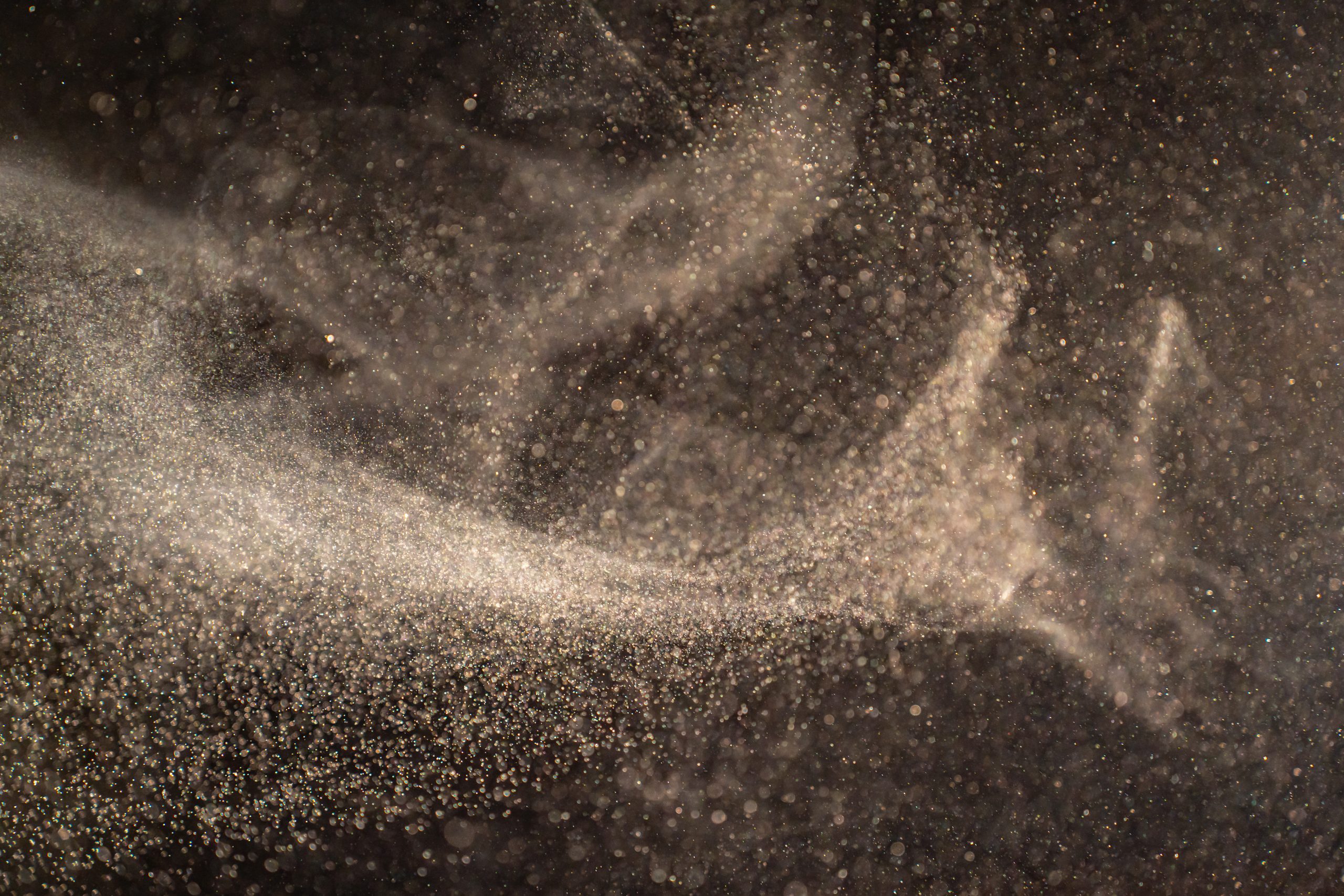 Organic dust particles floating on a light beam on black background.